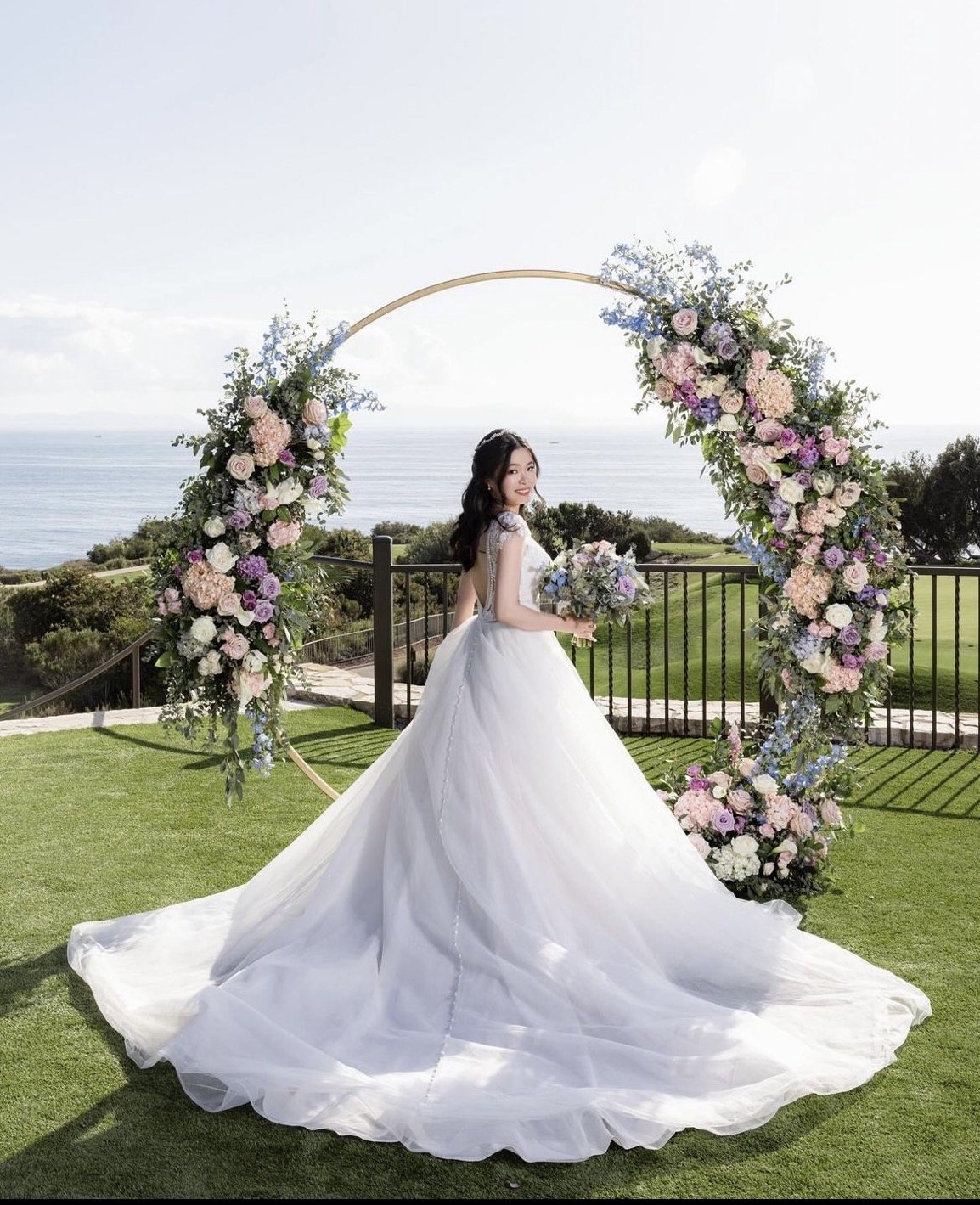 Bride beside a circular floral moon-gate arch on a coastal bluff