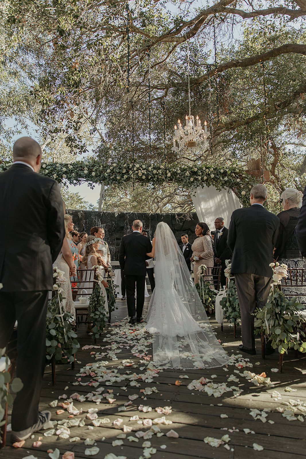 Petal-strewn wedding ceremony aisle under an arbor