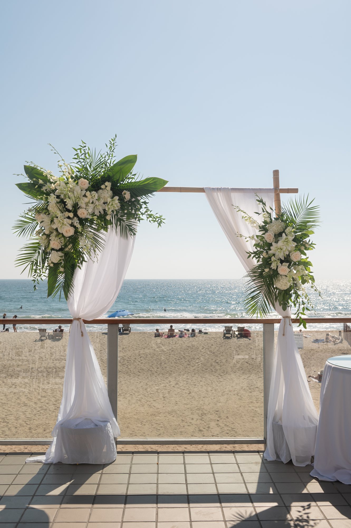 Beachfront wedding ceremony arch with white draping and florals